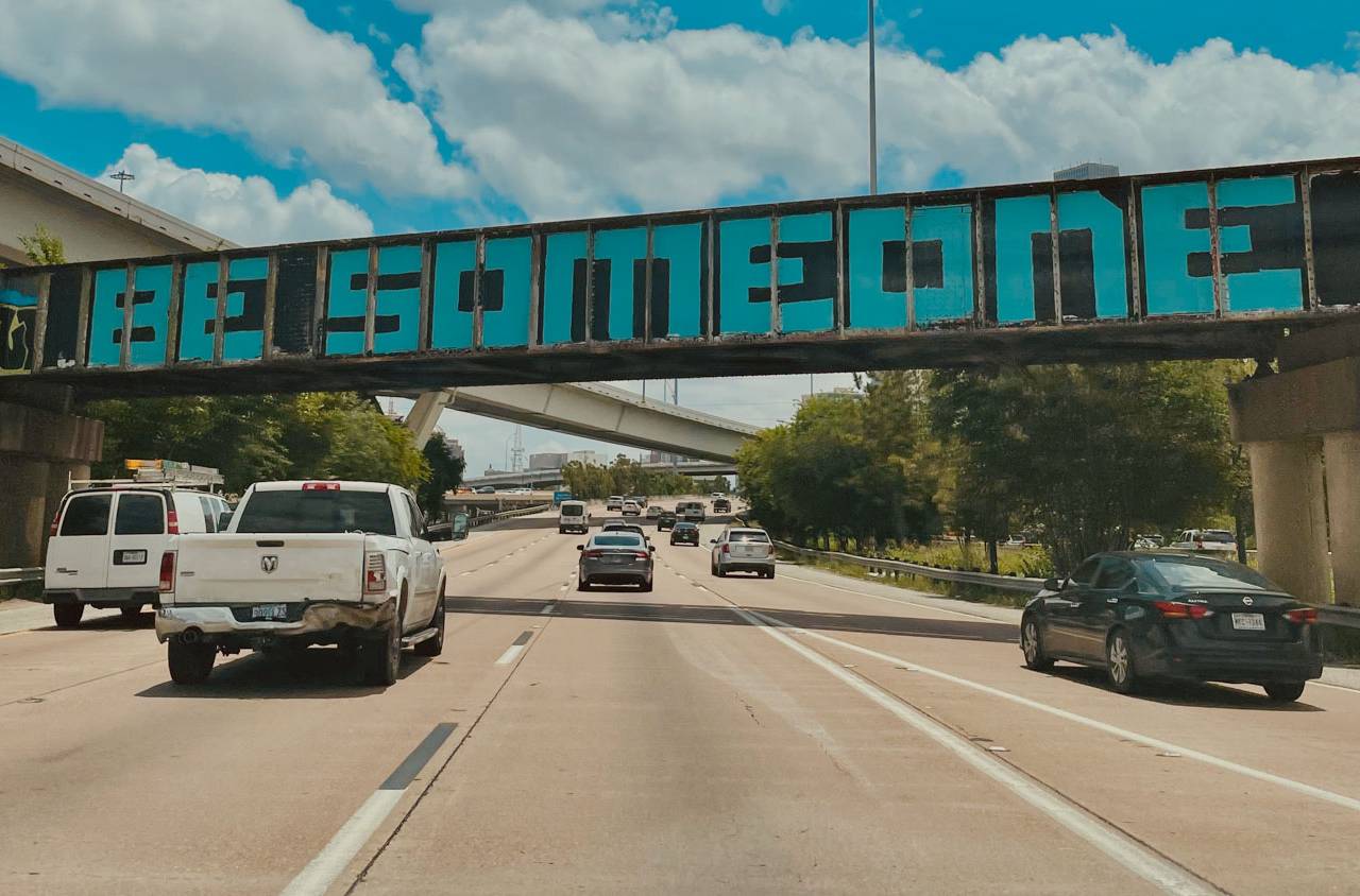 BE SOMEONE graffiti on a rail bridge over a Houston freeway